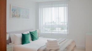 Habitación de hotel con cama, mesita de noche, ventana con persianas y un cuadro en la pared.