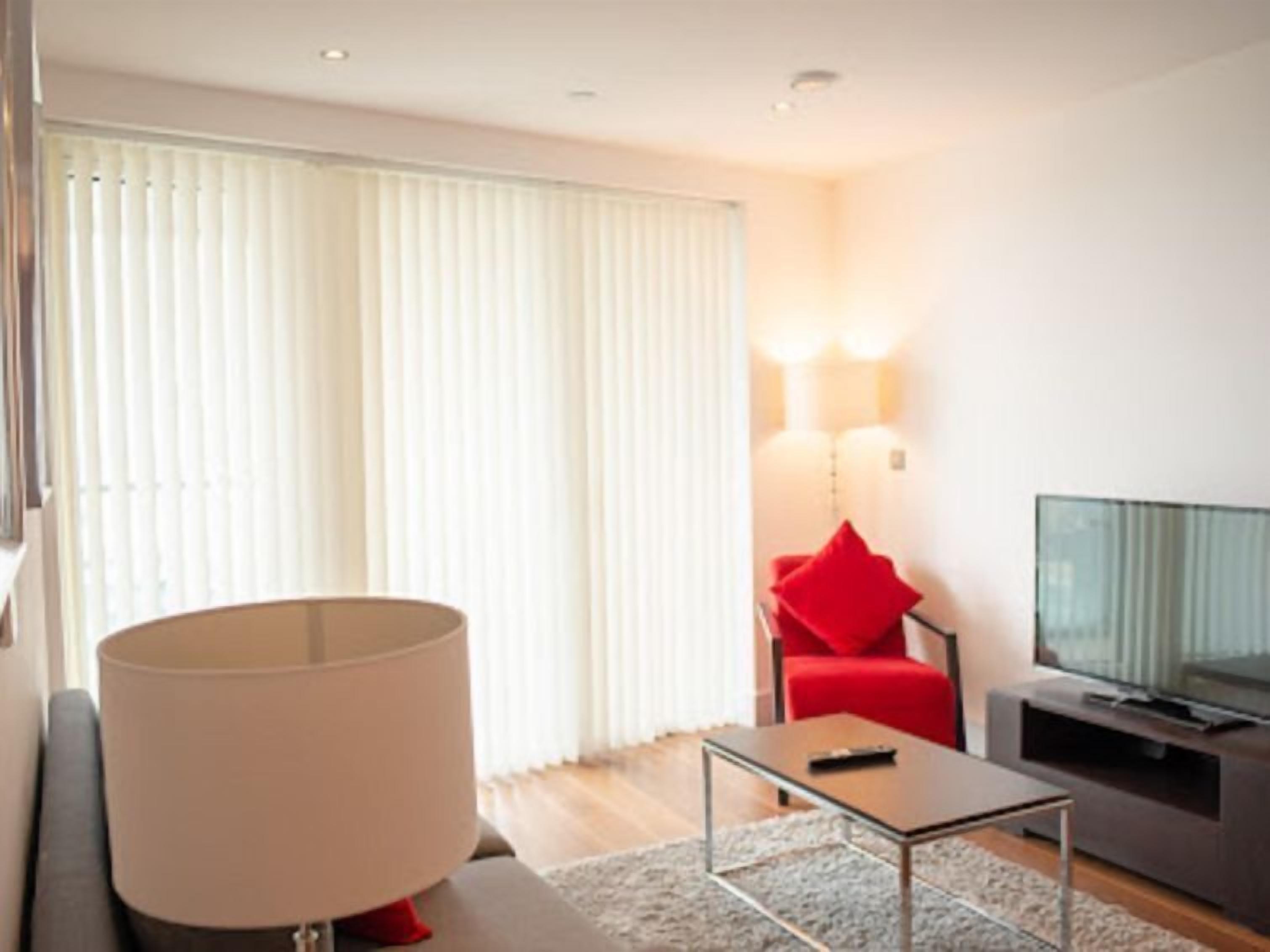 A modern living room with a sofa, a coffee table, a red chair, a television, and a large lamp.