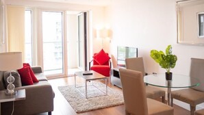 Una sala moderna con un sofá, una mesa de centro de vidrio y una silla roja. Hay un televisor y una planta en la habitación.