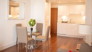 Una cocina moderna con armarios blancos, un comedor con mesa y sillas de vidrio, y un espejo en la pared.