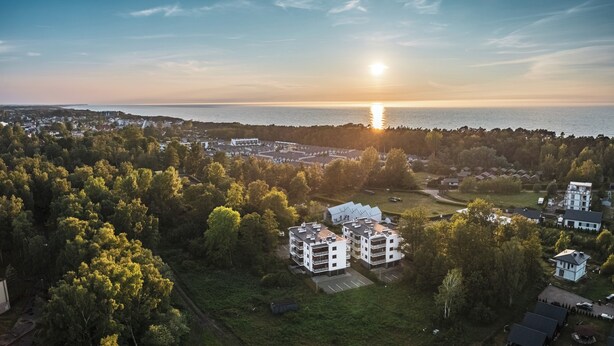 Vue aérienne d’un quartier résidentiel avec des bâtiments modernes, un ciel dégagé et un coucher de soleil sur l’eau.