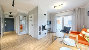 Un salon moderne avec un canapé, une table à manger pour deux personnes, un téléviseur fixé au mur et un balcon avec vue.