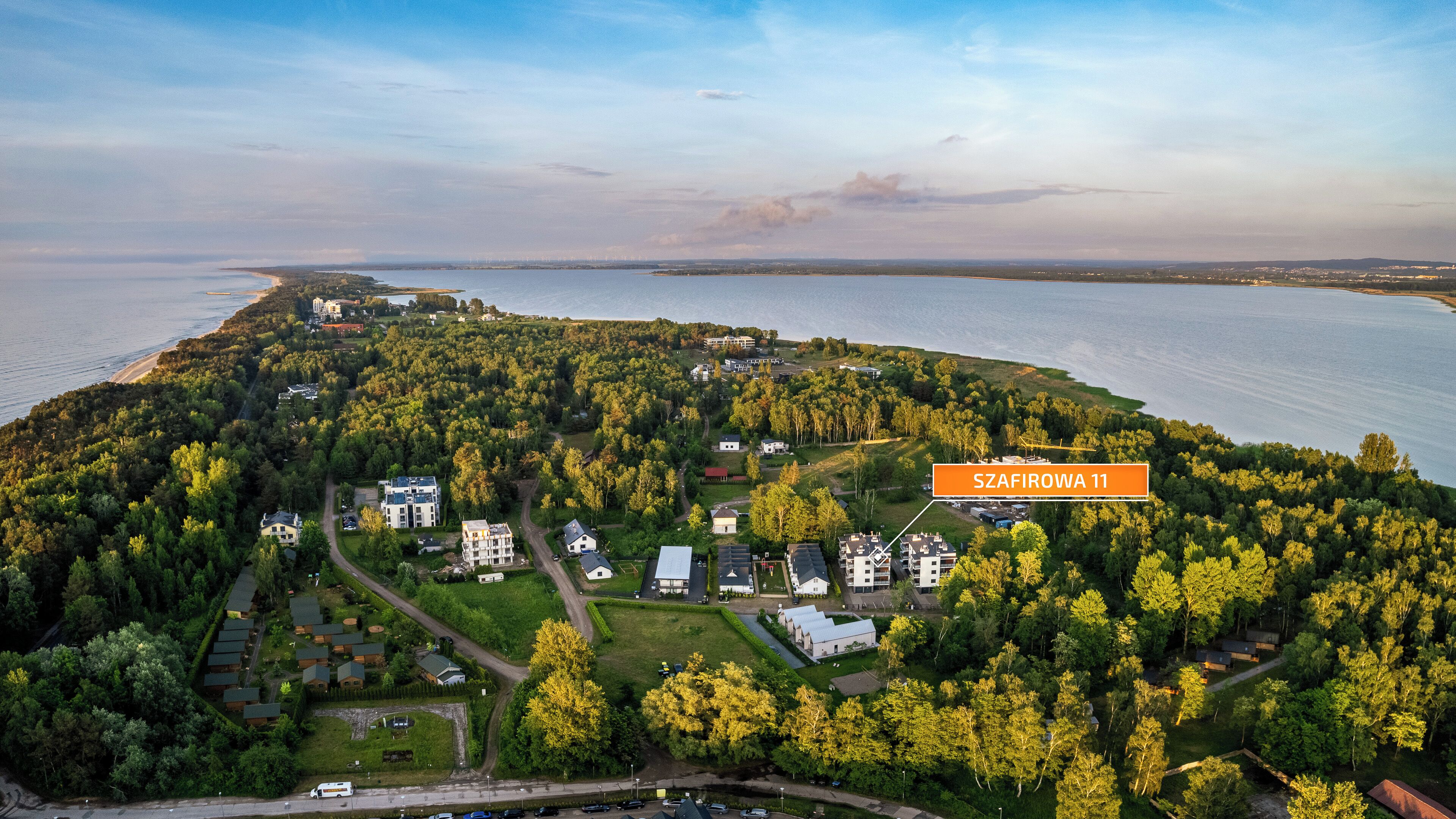 An aerial view of a residential area with multiple houses, a large body of water, and a label indicating "SZAFIROWA 11".
