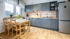 Une cuisine moderne avec des meubles gris, un réfrigérateur en acier inoxydable et une table à manger en bois, assortie de chaises.