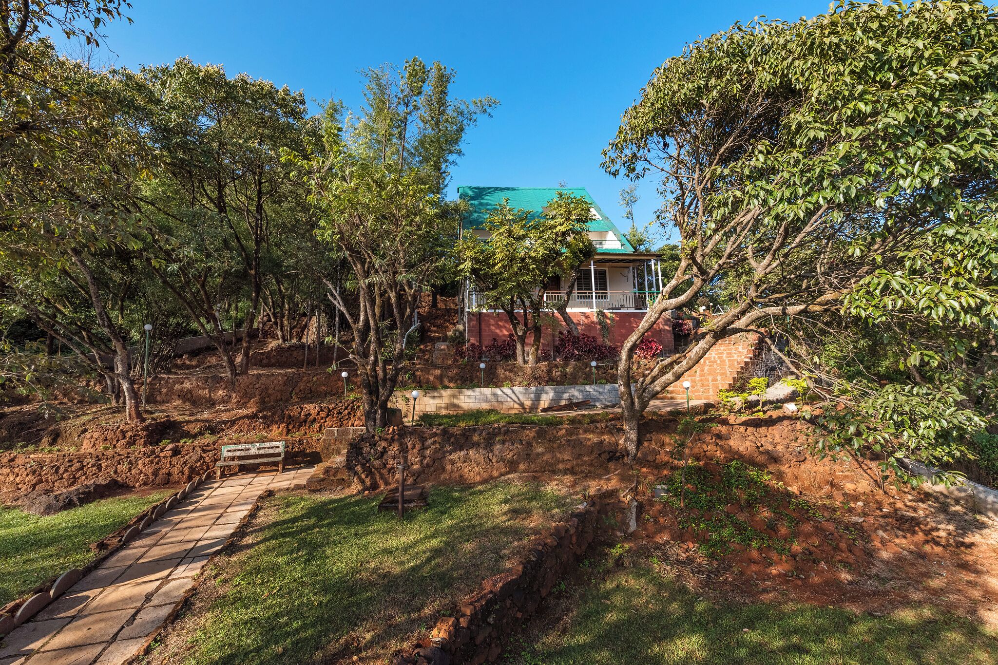 A house with a green roof, surrounded by trees and a stone pathway.