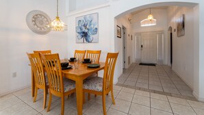 Un comedor con una mesa y sillas de madera, un reloj en la pared y un pasillo que conduce a otra habitación.