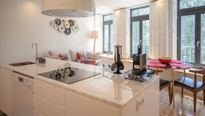 Une cuisine moderne dotée d’un îlot central, d’un coin repas avec une table et des chaises, et d’un canapé agrémenté de coussins colorés.