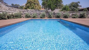 Une piscine rectangulaire à l’eau d’un bleu cristallin, entourée d’une terrasse en bois et d’un mur en pierre.