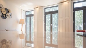 Une chambre avec un grand lit, deux fenêtres et une lampe fixée au mur.