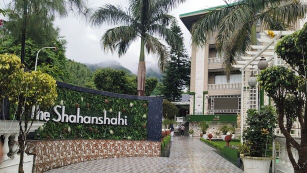Entrada de hotel com uma placa indicando "The Shanshahi", degraus levando à entrada e um jardim ajardinado com plantas em vasos.