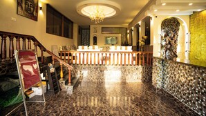 Um hall espaçoso com piso de mármore, uma escadaria imponente, um lustre e uma estátua de Buda.