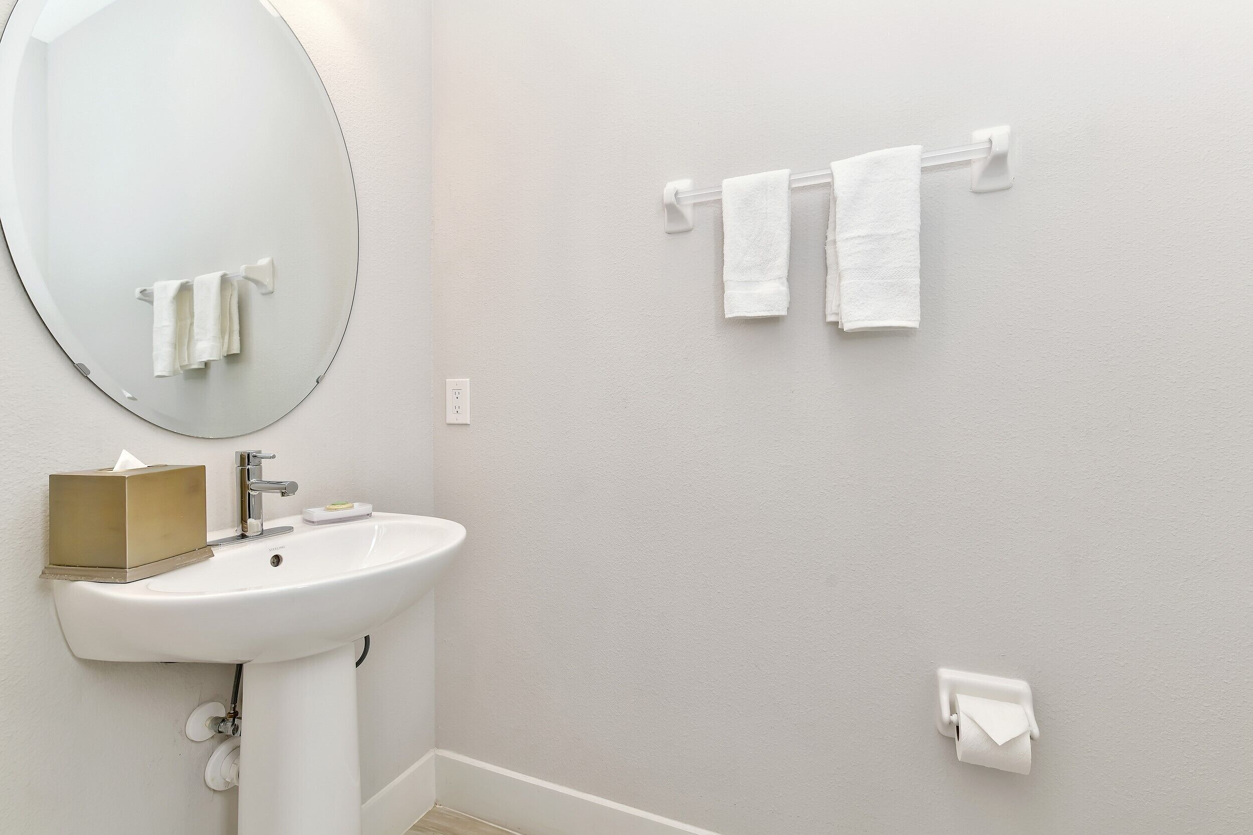 Une salle de bain avec un lavabo blanc, un miroir, deux serviettes posées sur un porte-serviettes mural et un porte-rouleau de papier toilette.