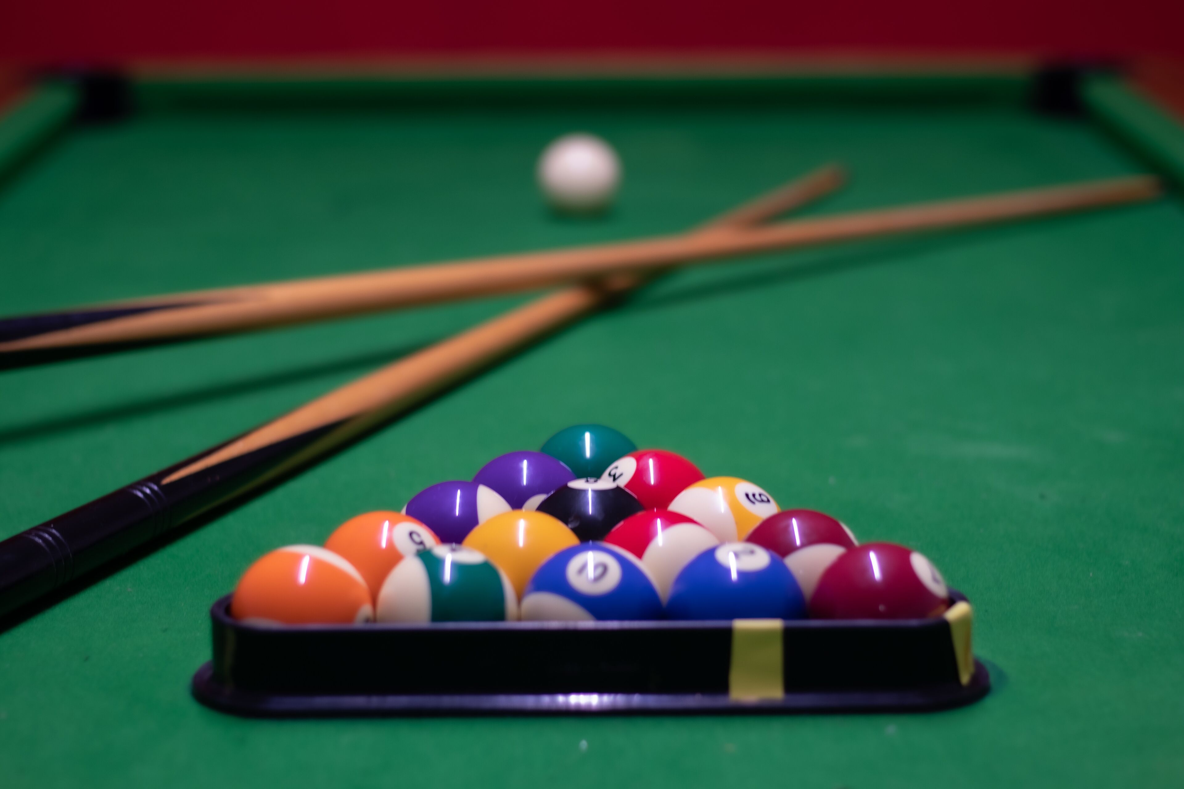 A pool table with a rack of billiard balls and two pool cues.