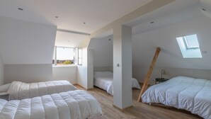 A modern, well-lit bedroom with two beds, a skylight, and a view of the outdoors.