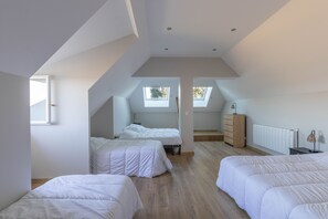 Une chambre spacieuse située dans les combles, avec deux lits, des fenêtres de toit, un radiateur et une armoire en bois.