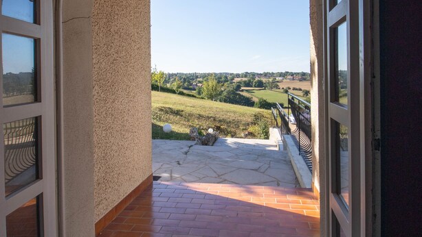 An arched doorway leading to a balcony with a clear view of a green landscape.