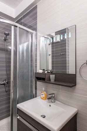 A bathroom with a shower, a sink, a mirror, and a soap dispenser. - Albania Dream Beachfront Apartment (Sarandë)