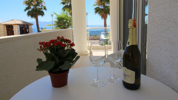 A table with a bottle of wine, two wine glasses, and a potted plant on a balcony overlooking the sea. - Albania Dream Beachfront Apartment (Sarandë)
