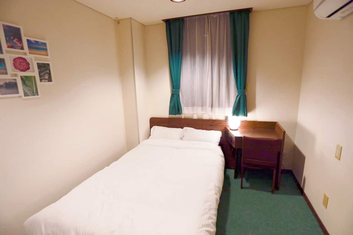 Una habitación pequeña y ordenada con una cama individual, un escritorio y una silla.