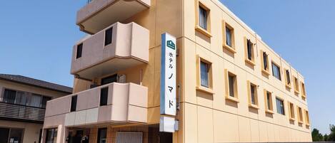A multi-story hotel with a beige facade, a balcony on the second floor, and a sign indicating it is a hotel.