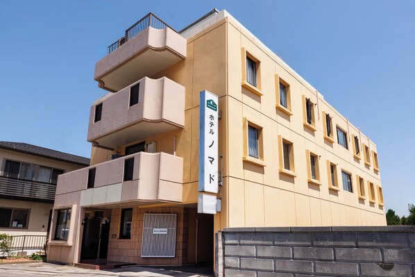 A multi-story hotel with a beige facade, a balcony on the second floor, and a sign indicating it is a hotel.