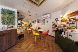 A cafe with a wooden herringbone floor, a green wall with plants, and colorful chairs.
