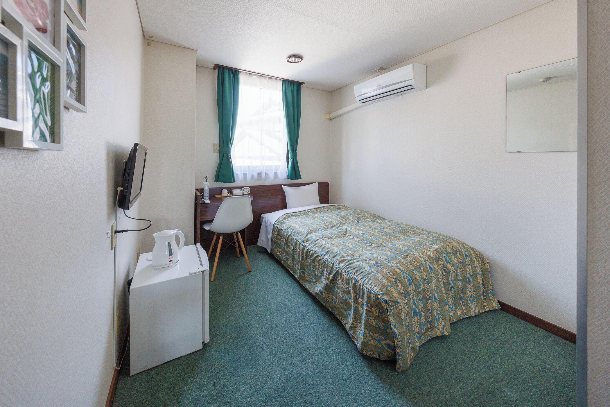 A compact hotel room with a single bed, a desk with a chair, a small refrigerator, and a television.