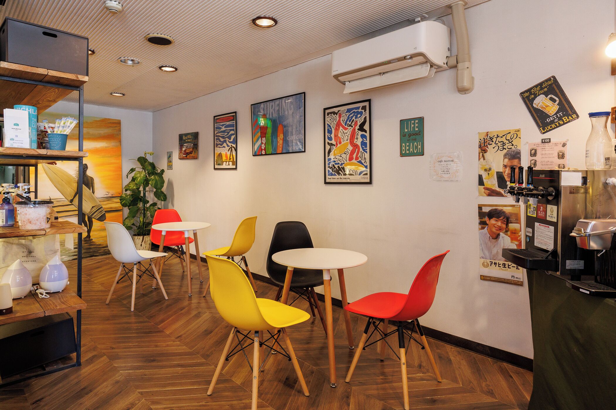 Interior de una cafetería con suelo de madera, sillas de colores y obras de arte en las paredes.