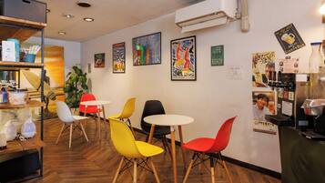 Interior de una cafetería con suelo de madera, sillas de colores y obras de arte en las paredes.