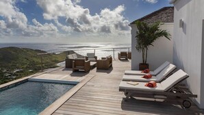 Eine Holzterrasse mit Liegestühlen und einem kleinen Pool mit Blick auf die Küste.
