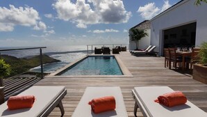 Ein Poolbereich mit Liegestühlen, einem Esstisch und Blick auf den Ozean.