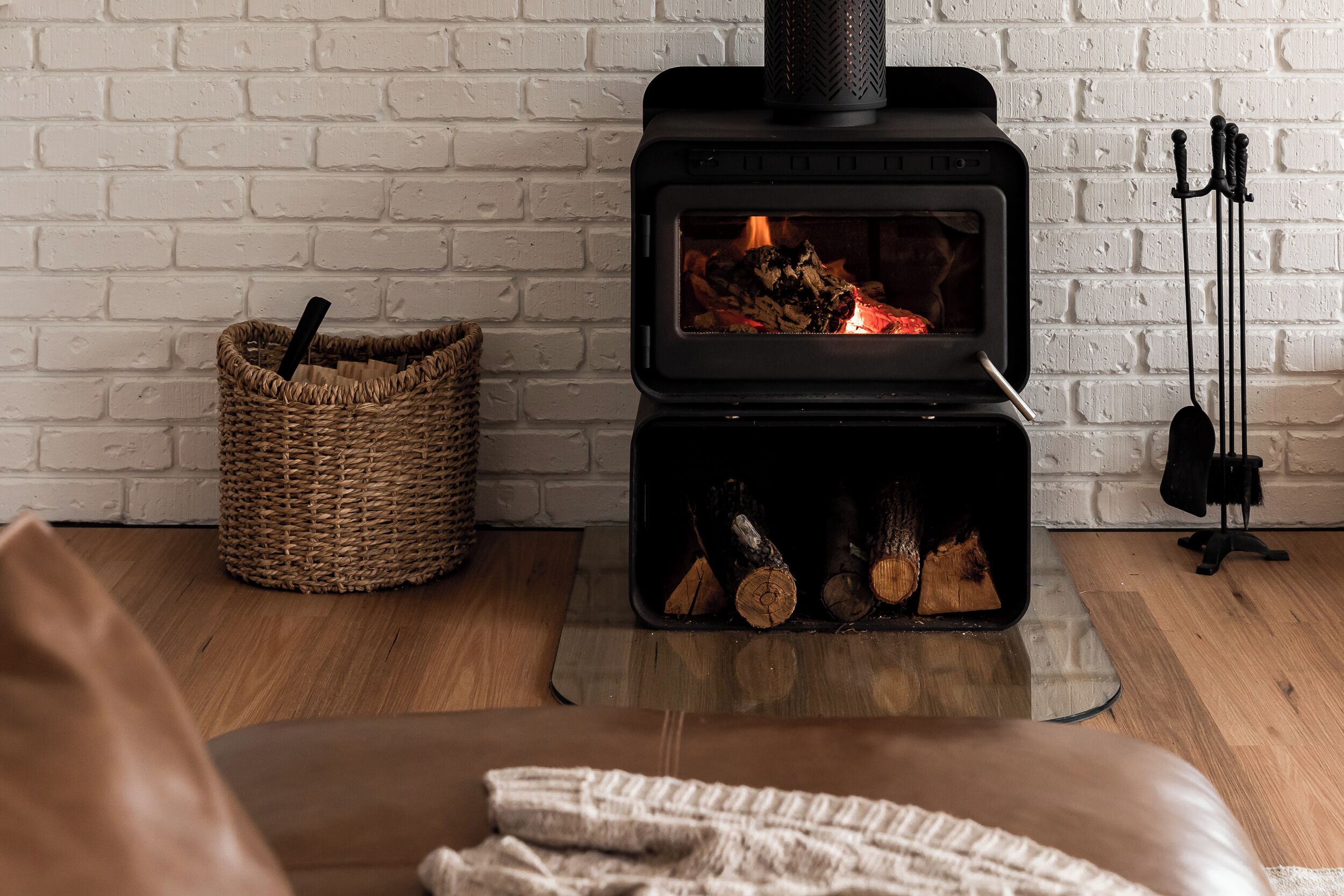 Una habitación acogedora con una estufa de leña, una cesta de mimbre y un atizador para la chimenea.