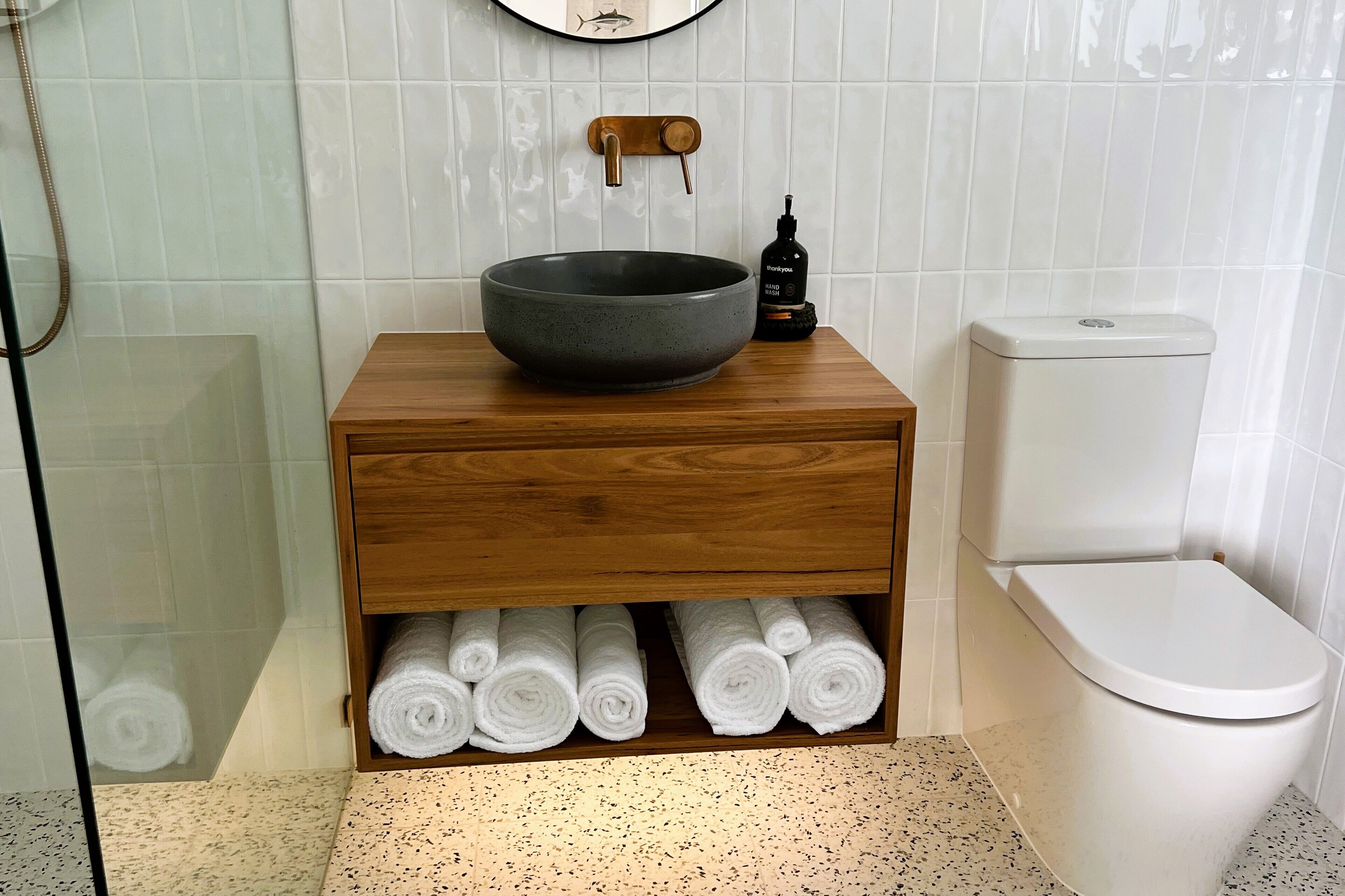 Une salle de bain avec un meuble-lavabo en bois, un grand lavabo en forme de cuve, des toilettes et un porte-serviettes avec des serviettes.