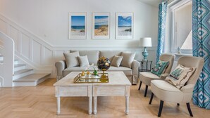 Una sala de estar con un sofá, sillones, una mesa de centro con adornos, un globo terráqueo y fotografías enmarcadas de la playa en la pared.