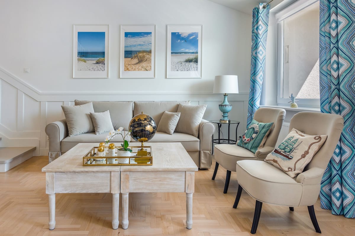 Ein Wohnzimmer mit einer Couch, Sesseln, einem Couchtisch mit Dekoration, einem Globus und gerahmten Bildern vom Strand an der Wand.