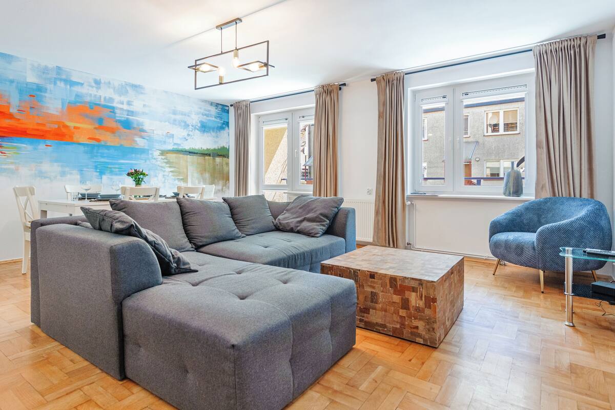Ein modernes Wohnzimmer mit einem Ecksofa, einem Glastisch und einem blauen Sessel.