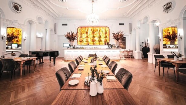 Un comedor espacioso con una larga mesa de madera, rodeada de sillas, y un piano al fondo.