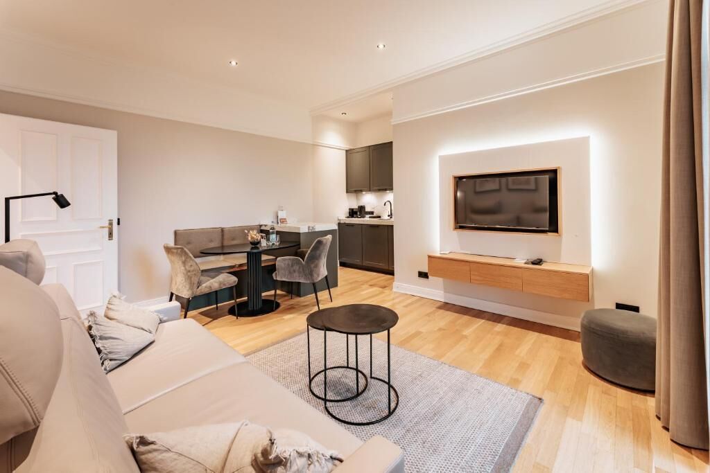Una sala moderna con un sofá, comedor, cocina y televisor montado en la pared.