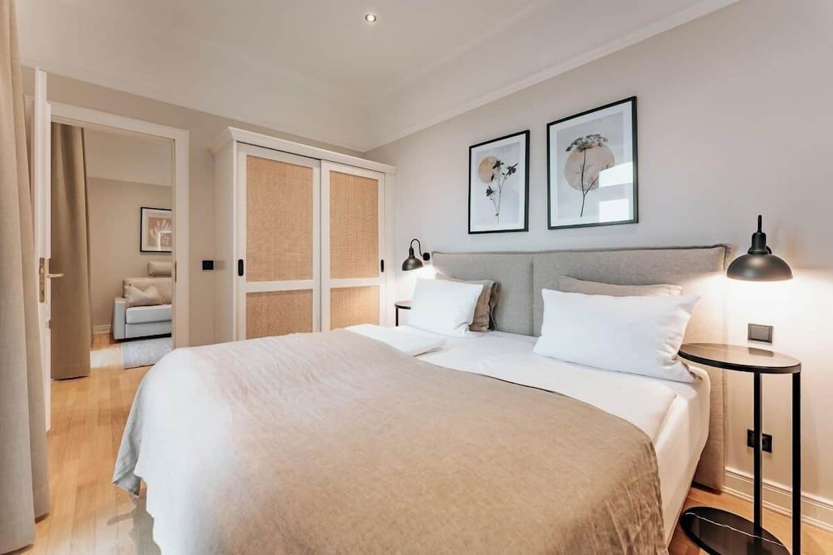 Un dormitorio moderno con una cama grande, una mesita de noche con lámpara y dos cuadros enmarcados en la pared.