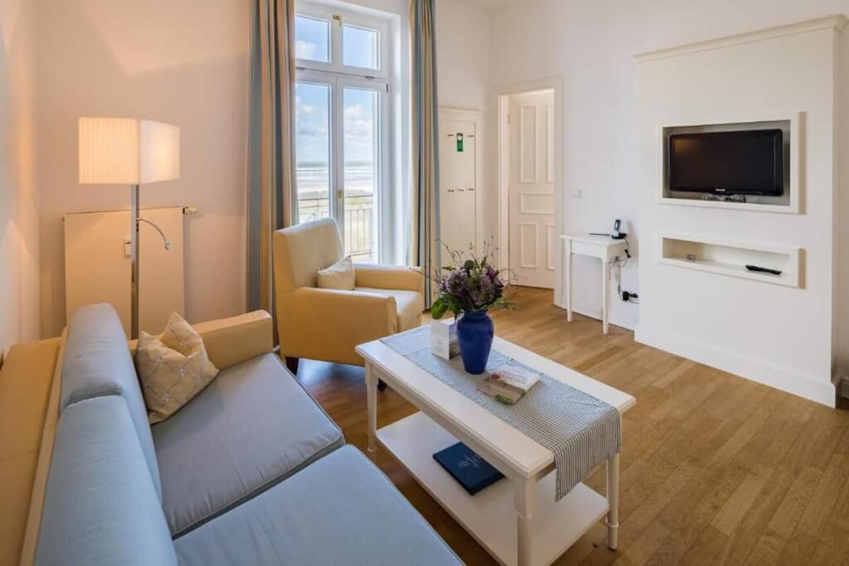 Una habitación de hotel moderna con sofá, sillón y una mesita con un florero.