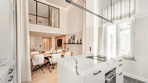 Una cocina moderna con una isla de mármol, horno empotrado y una zona de comedor con mesa y sillas de madera.