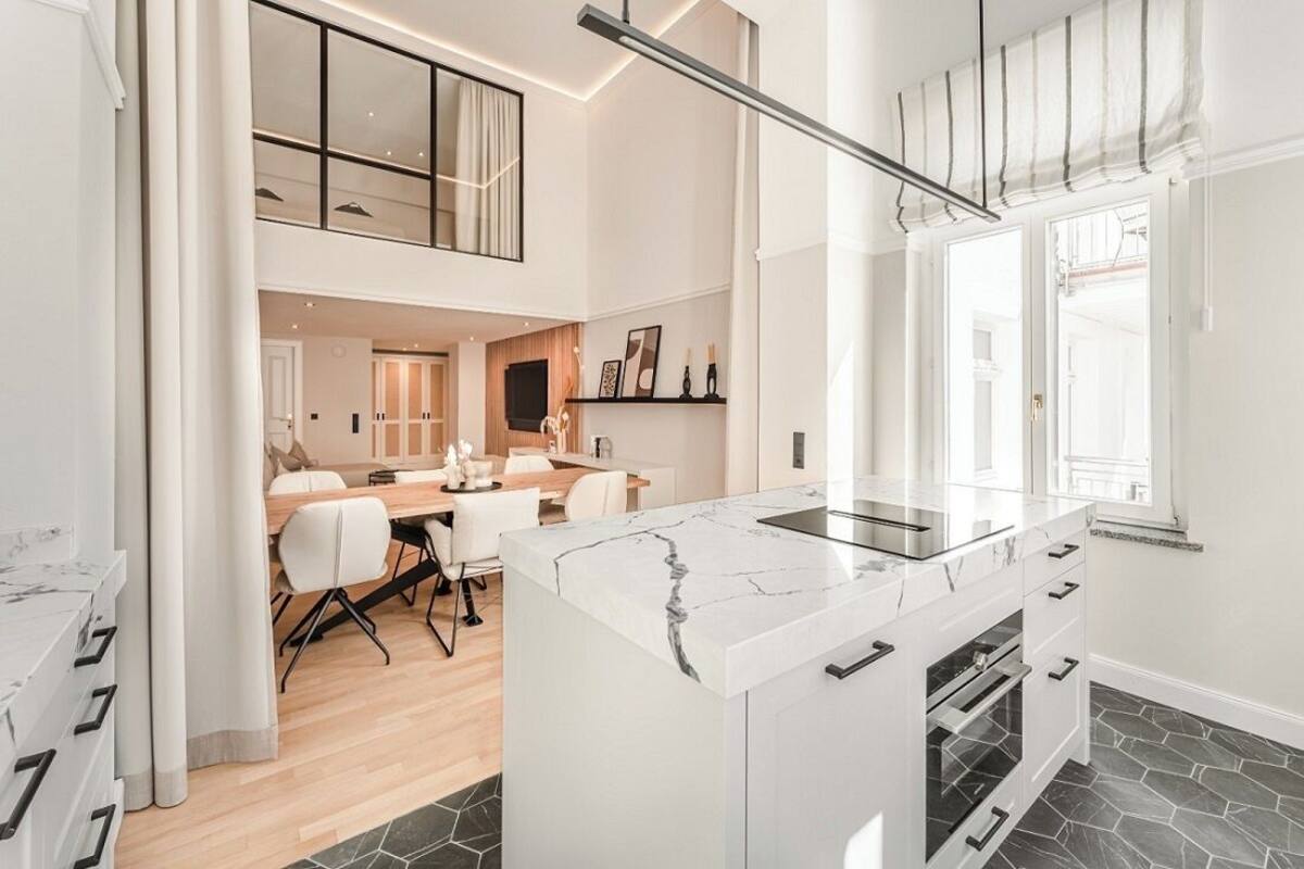 Una cocina moderna con una isla de mármol, horno empotrado y una zona de comedor con mesa y sillas de madera.