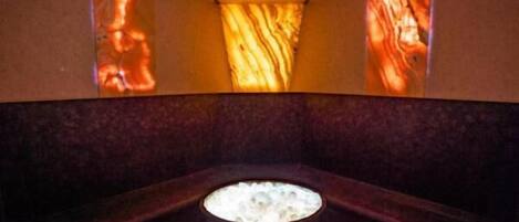 A spa area with a central hot tub surrounded by dark seating and illuminated walls.