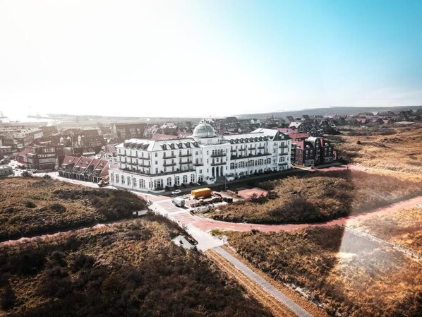A large, multi-story building with a prominent dome, surrounded by a landscaped area with pathways and sparse vegetation. - Strandhotel Kurhaus Juist (Juist)