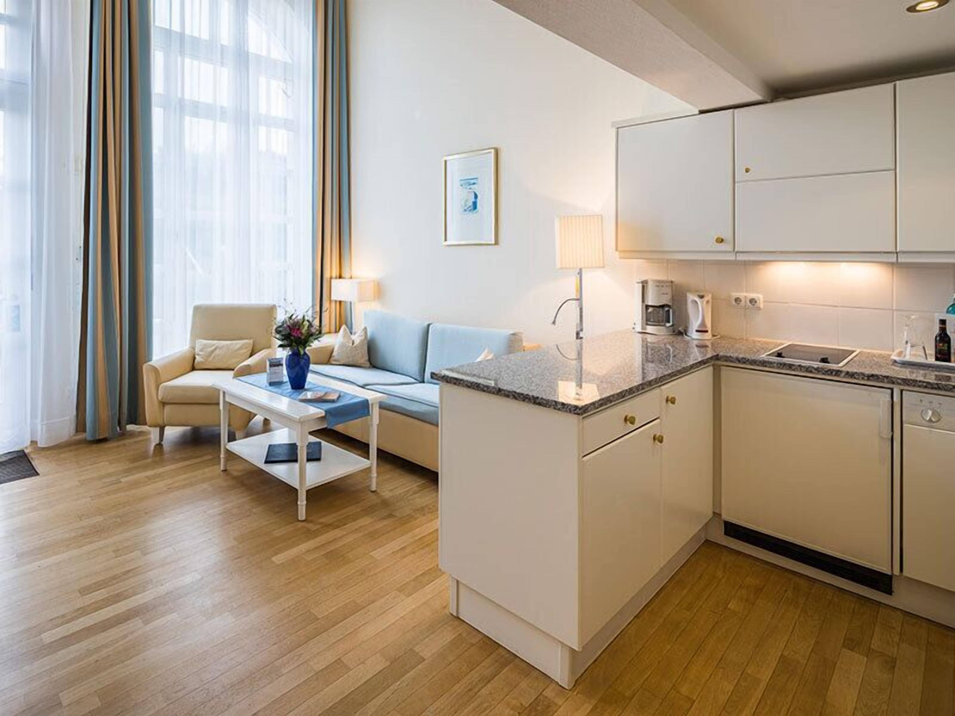 A modern hotel room with a sofa, coffee table, and a small kitchen area.