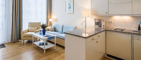 A modern hotel room with a sofa, coffee table, and a small kitchen area.