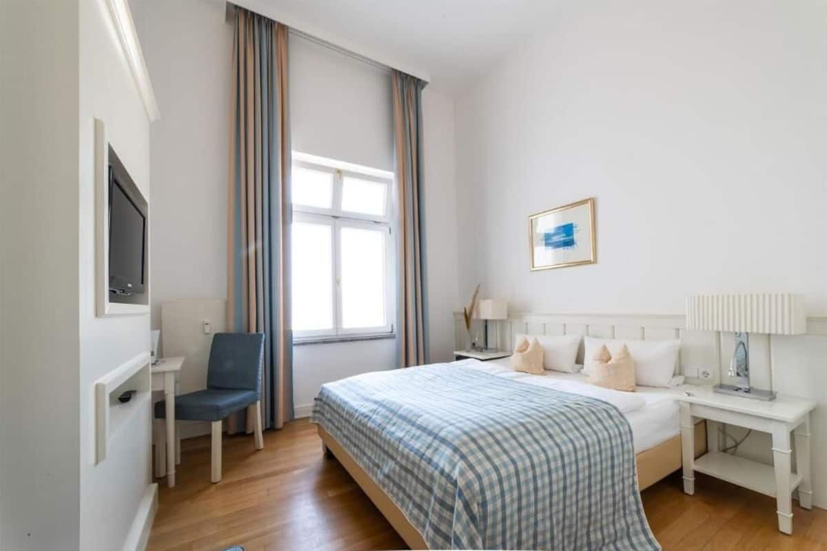 Habitación de hotel con cama, escritorio, silla, televisión y ventana con cortinas.