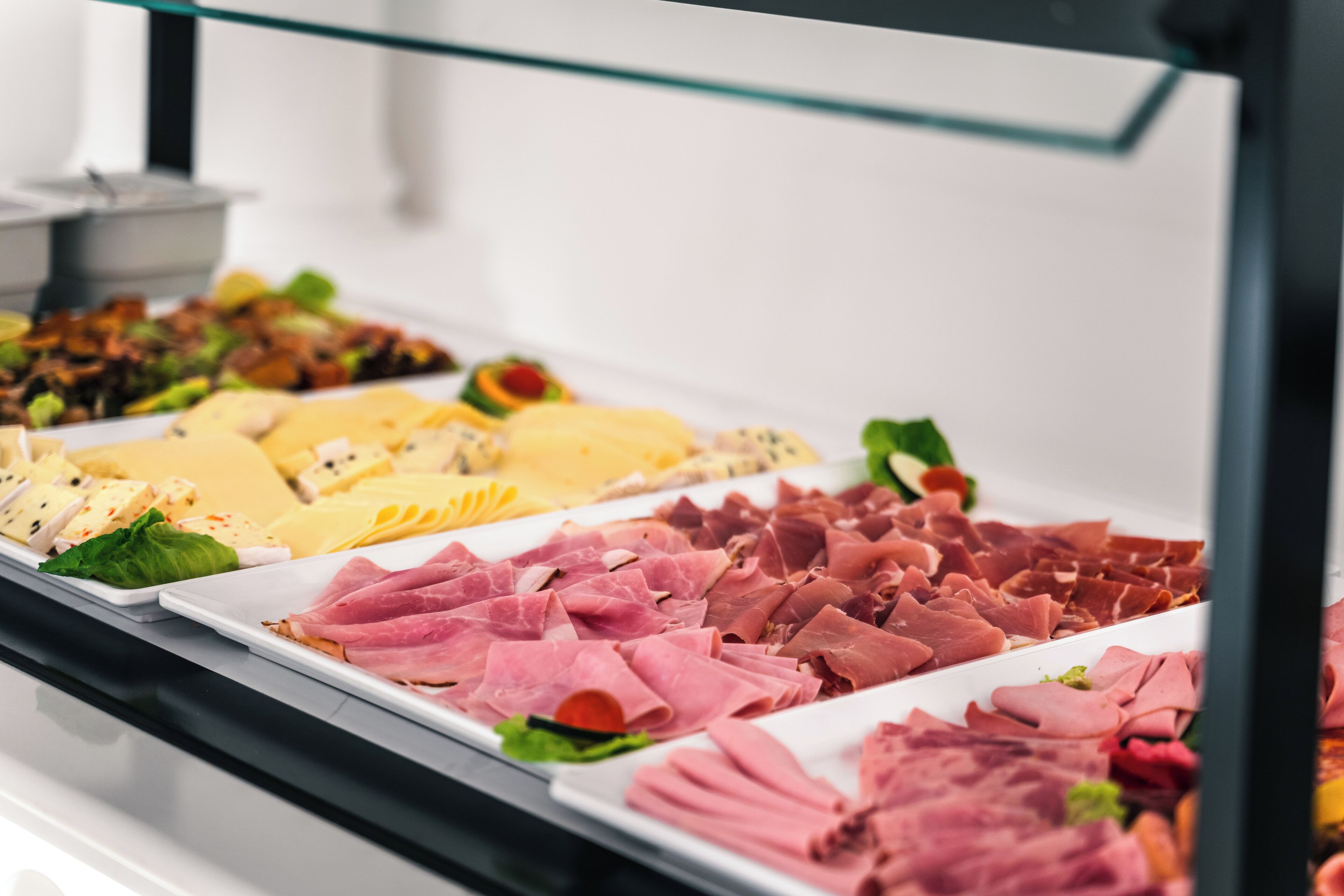 A buffet with various types of cheeses, meats, and vegetables.