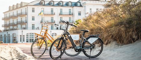 Deux vélos sont garés sur un chemin de sable, avec un bâtiment en arrière-plan.