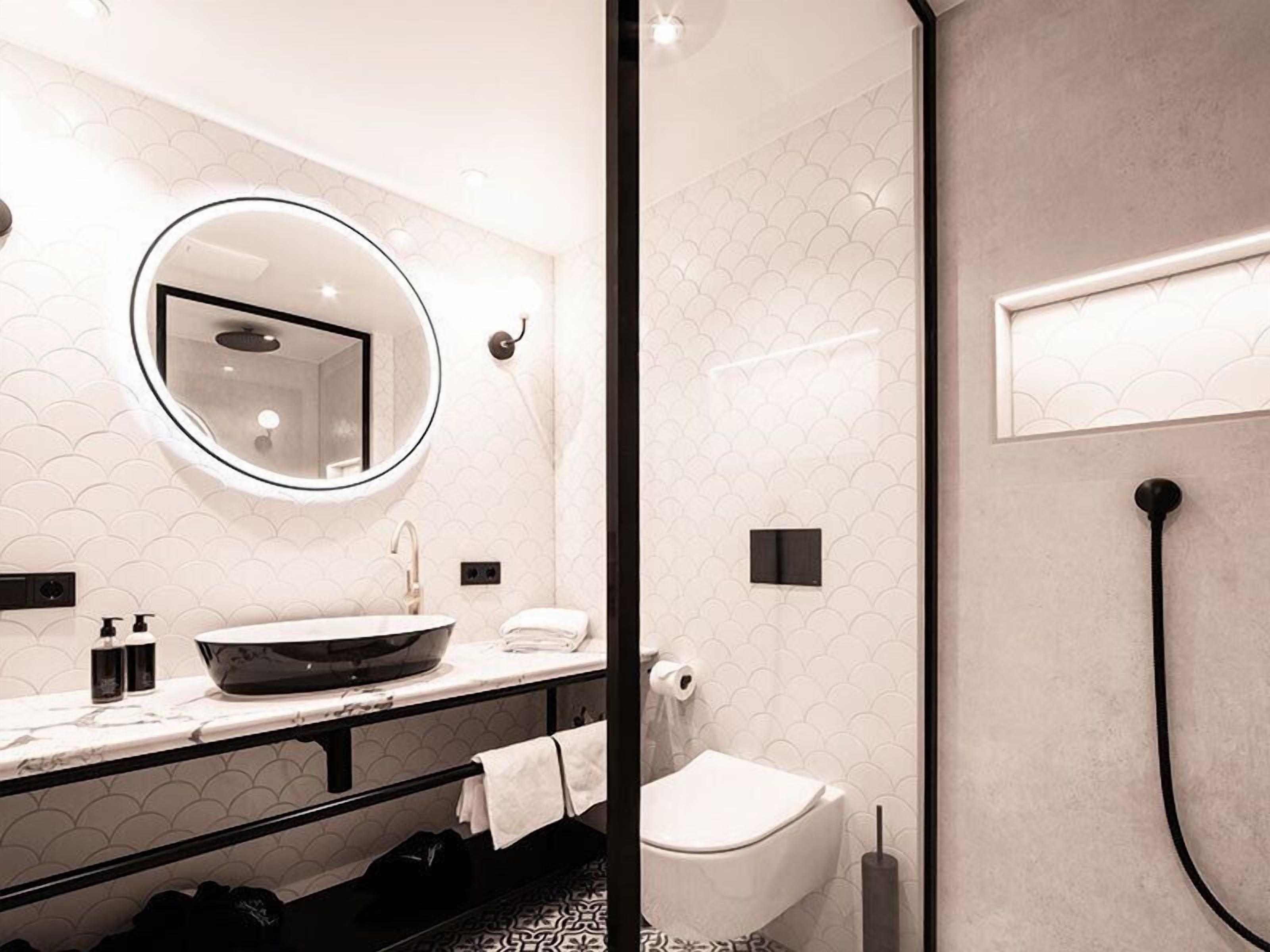 Un bany modern amb un mirall rodó, un lavabo de sobretaula, un vàter i un raig de dutxa.